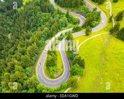 Gekrümmte Asphaltwege schlängeln sich durch üppige grüne Wälder in den Alpen und bieten atemberaubende Ausblicke und eine aufregende Fahrt. Diese Luftperspektive fängt die Schönheit eines Roadtrips im Sommer ein. Stockfoto