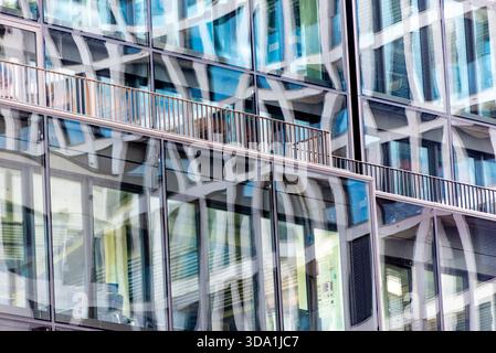 Verzerrte architektonische Reflexionen auf einer modernen Glasfassade in der Nähe des Alexanderplatzes in Berlin. Abstraktes geometrisches Stadtmuster mit Balkondetails Stockfoto