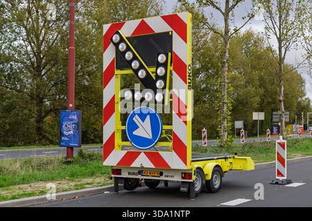 Mobiler Pfeilanhänger mit hellen LED-Leuchten, die den Verkehr auf eine zu wartende Straße lenken. Autobahnszene mit Sicherheitsmarkierungen und Bauschildern. Stockfoto