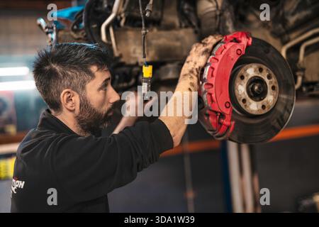 Rom, italien 20. november 2025: Professioneller Mechaniker überprüft roten Bremssattel und Bremsscheibe in der Werkstatt, fettbedeckte Hände mit Schwerpunkt auf Präzisionswartung Stockfoto