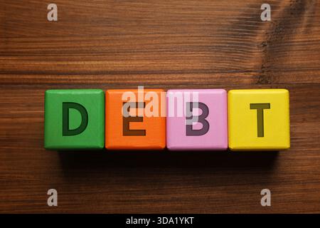 Schuldenwort aus Würfeln mit Buchstaben auf Holztisch, Draufsicht Stockfoto