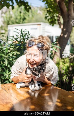Eine Frau mittleren Alters hält eine kleine schwarz-weiße Katze im Arm Stockfoto