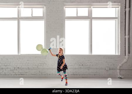 Glückliches Mädchen, das drinnen mit grünen Ballons und gestreiften Socken läuft Stockfoto