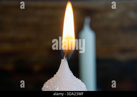 Eine Nahaufnahme einer weißen Kerze, die sanft brennt, mit detaillierter Wachsstruktur und einer glühenden Flamme. Stockfoto