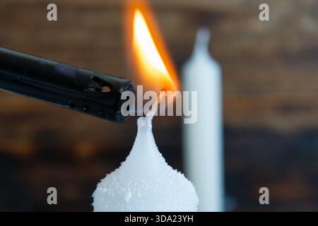 Eine detaillierte Makroaufnahme erfasst den Moment, in dem ein Kerzendocht entzündet wird, während ein langes schwarzes Feuerzeug eine warme Flamme erzeugt. Stockfoto