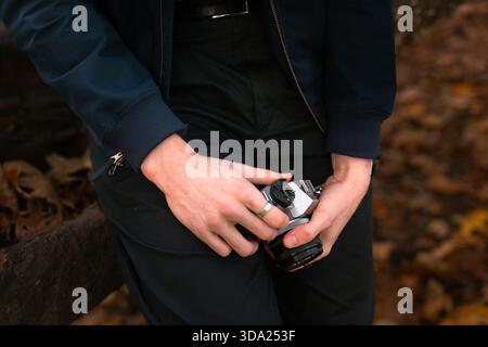 Person mit Kamera, während sie im Herbst auf einem Baumstamm in einem Wald sitzt Stockfoto