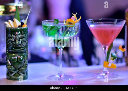 Drei bunte Cocktails in einzigartigen Gläsern auf einer Bartheke. Stockfoto