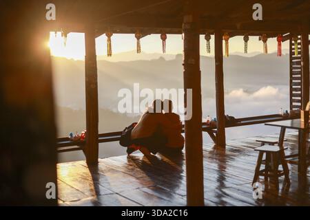 Romantisches Paar Silhouette Genießen Sie den Sonnenuntergang auf den Berg zusammen. Friedlicher Moment der Liebe im Reiseurlaub, heiter und intim auf Holzbalken Stockfoto