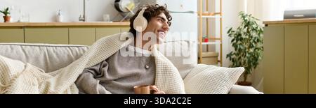 Ein hübscher junger Mann sitzt in seiner Wohnung, schlürft einen Drink und genießt Musik, Banner Stockfoto