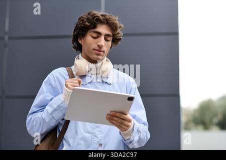 Junger Mann im Freien, mit Tablet und Kopfhörern in einer urbanen Umgebung. Stockfoto