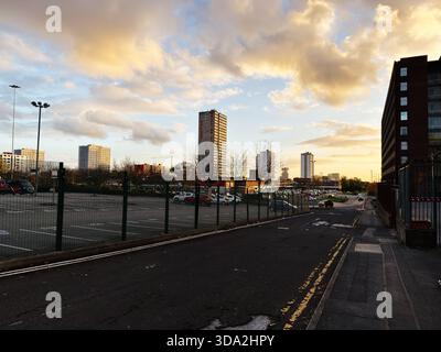 Salford, Vereinigtes Königreich - 8. November 2025: Eine Stadtstraße und ein Parkplatz unter einem goldenen Sonnenuntergang mit hohen Gebäuden in Salford. Stockfoto