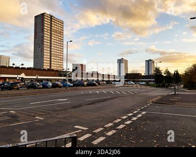 Salford, Vereinigtes Königreich - 8. November 2025: Stadtstraße in Salford mit einem hohen Turm, Geschäften, parkenden Autos und einem hellen Himmel. Stockfoto