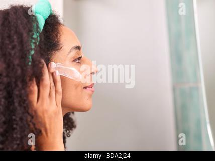Porträt Einer Frau, Die Während Der Morgendlichen Hautpflegeroutine Bei Der Selbstpflege Zu Hause Hautpflegecreme Auf Die Wange Aufträgt Stockfoto