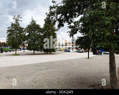 Salford, Großbritannien - 8. November 2025: Urban plaza Szene in Salford mit Bäumen, Autos und Geschäften unter bewölktem Himmel. Stockfoto