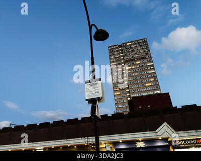 Salford, Vereinigtes Königreich - 8. November 2025: Ein hohes Hochhaus dominiert eine Salford Street mit Lampenpfosten und Ladenfronten unter blauem Himmel. Stockfoto