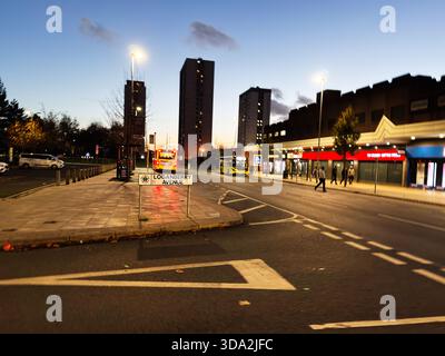 Salford, Großbritannien - 08. November 2025: Geschäftige Stadtstraße in Salford mit Bussen, Einkaufsmöglichkeiten und Ladenfronten in der Abenddämmerung. Stockfoto