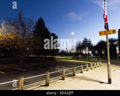 Salford, Großbritannien - 08. November 2025: Ruhiger Abend in Salford mit Park, Fahnenmast, Straßenlaternen und Verkehrsschildern. Stockfoto