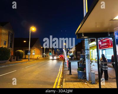Salford, Großbritannien - 8. November 2025: Geschäftige Stadtstraße in Salford mit Friseur, Fußgängern und leuchtenden Ladenfronten. Stockfoto
