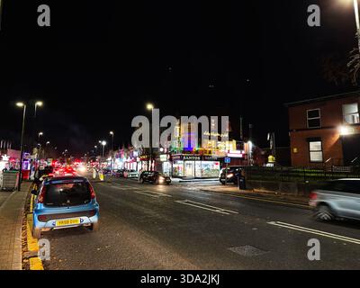 Salford, Großbritannien - 8. November 2025: Nachtszene auf einer lebhaften Salford Street mit Neonschildern, Verkehr und Fußgängern. Stockfoto