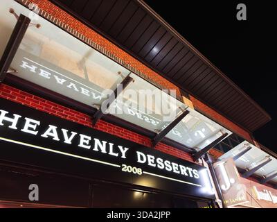 Salford, Großbritannien - 8. November 2025: Nachtszene eines Backsteindessertgeschäfts in Salford mit einem hellen Himmlischen Desserts-Schild. Stockfoto