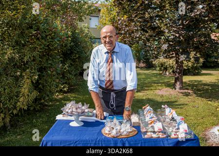 Senior Mann lächelt, steht hinter seinem Marktstand mit Keksen und Süßigkeiten Stockfoto
