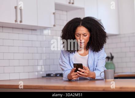 Neugierige Frau benutzt das Smartphone am Küchenschalter in ungezwungener Morgenstimmung Stockfoto