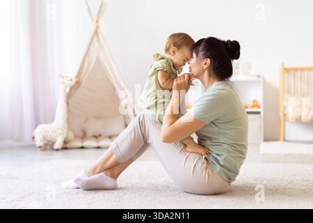 Mutter sitzt auf dem Boden und hält ihr Baby nahe, während sie die Stirn berühren Stockfoto