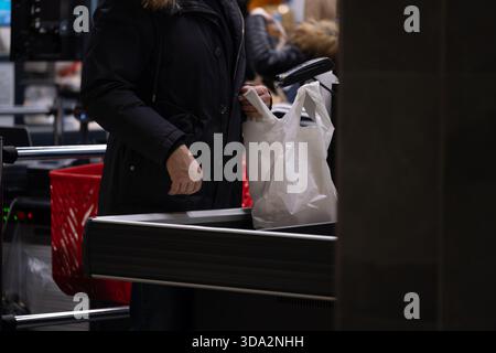 Mann, der an einer Supermarktkasse für Lebensmittel bezahlt, mit einem Barcode-Scanner und einer Plastiktasche. Die Szene repräsentiert den modernen Einzelhandel, den täglichen Konsum Stockfoto