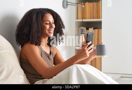 Frau Lächelt Beim Selfie-Nehmen Mit Telefon Und Kaffeetasse Zu Hause Stockfoto