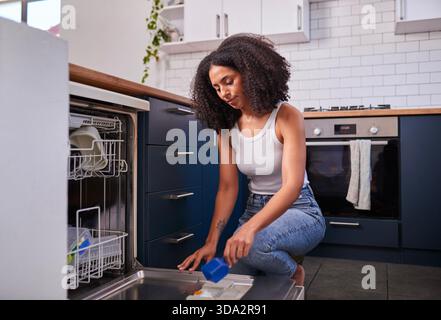 Junge Frau Kniend Am Offenen Geschirrspüler In Der Modernen Küche, Tut Geschirr Und Tägliche Hausaufgaben Stockfoto