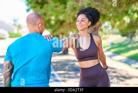 Freundlicher Outdoor-Workout-Moment: Kombinieren Sie High-Fiving und Lächeln während der Park Fitness Session zusammen bei Sonnenlicht Stockfoto