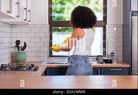 Frau, die Geschirr in der modernen Küche mit gelben Handschuhen und Jeans wäscht Stockfoto