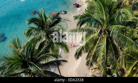 Atemberaubende Aussicht auf ruhige Strände auf Koh Kood Island, Thailand, mit Palmen, die weiche Sandstrände umrahmen. Ein Paar genießt einen friedlichen Spaziergang entlang der Küste, umgeben von lebhaftem türkisfarbenem Wasser. Stockfoto