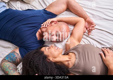 Glückliches Paar liegt auf dem Bett, lächelt und verbindet sich in zwanglosem Wohnkomfort Stockfoto