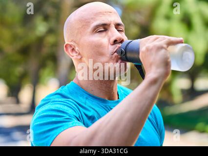 Glatzmann trinkt Wasser aus der Shaker-Flasche während des Outdoor-Workouts im Park Stockfoto