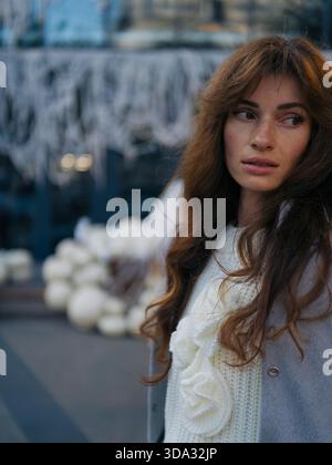 Detailgetreues Nahaufnahme-Porträt einer schönen Frau mit langen Haaren und Sommersprossen, die wegblickt, in weißem Strickpullover und grauer Jacke in weichem Herbstlick Stockfoto