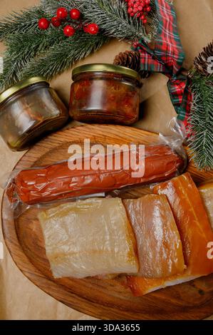 Geräucherte Fischstücke und getrocknete Wurst mit Butter auf Bastelpapier. Auswahl an Räucherfisch und Fleischprodukten mit Pflanzenöl auf einem Holztisch. Stockfoto