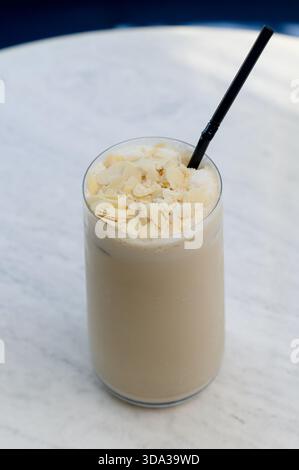 Hohes Glas Eislatte mit Mandelflocken. Nahaufnahme einer Vanille- oder Nussfrappe in einem klaren Glas Stockfoto