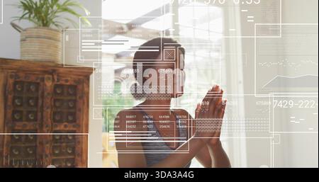 Betende Frau, die zu Hause in der Nähe des Fensters ein graues Tanktop trägt, mit über-Ohr-Kopfhörern und UI-Overlays Stockfoto
