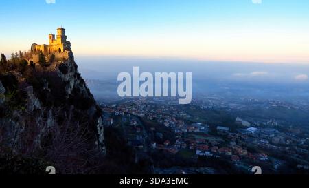 San Marino, 26.12.2014 Beschreibung: Guaita Fortress Tower bei Sonnenaufgang über dem nebeligen Stadtbild von San Marino Stockfoto