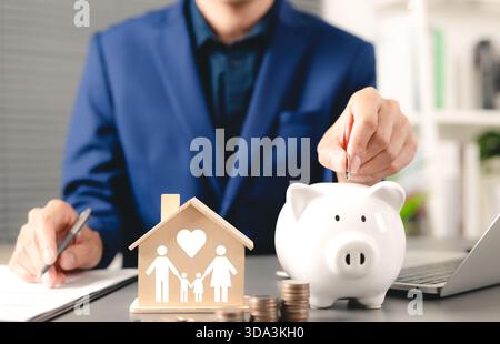 Familiensparkonzept. Geschäftsmann legt Münze in Sparkasse mit Holzhausmodell ein, das Familie und Liebe symbolisiert, Familienfinanzplanung Stockfoto