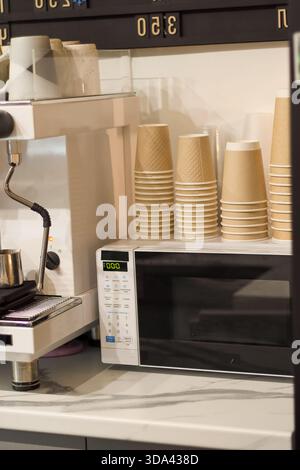Mehrere Stapel strukturierter Einwegbecher neben der Mikrowelle im Café Stockfoto