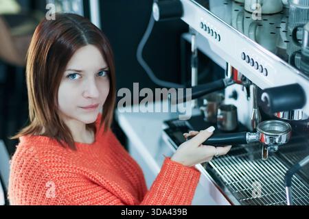 Der Barista in einem gemütlichen Strickpullover bereitet Kaffee mit Portafilter in Café-Umgebung sorgfältig zu Stockfoto