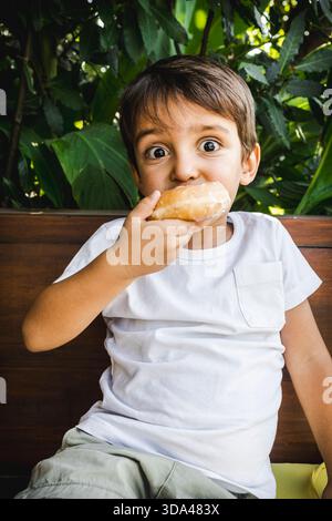 Entzückender 3-jähriger Junge, der einen Donut hält und genießt. Stockfoto