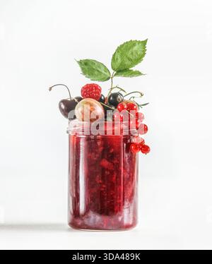 Rote Marmelade im Glas mit verschiedenen Beeren: Rote Johannisbeeren, Himbeere, Kirsche, Stachelbeere und grünes Blatt auf weißem Hintergrund. Konservierung von köstlichen Sommer fr Stockfoto