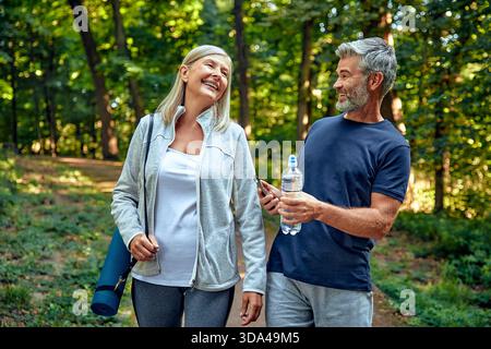 Ein fröhliches Paar schlendert auf einem landschaftlich reizvollen Wanderweg, der von lebhaftem Grün umgeben ist und durch unterhaltsame Outdoor-Aktivitäten Gesundheit und Wellness fördert Stockfoto
