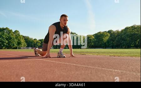 Geballter junger Mann in Startposition auf der Stadionbahn, bereit zum Sprint. Konzept: Motivation, Disziplin, Sport, Leichtathletik, Zielsetzung, Enduranc Stockfoto