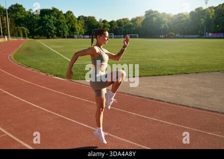 Sportliche Frau in Aktivkleidung, die im Morgenlicht hohe Knie auf der Stadionbahn macht. Konzept: Motivation, Fitnesstraining, gesunder Lebensstil, Karte Stockfoto