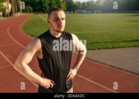 Porträt eines jungen muskulösen Mannes, der nach dem Training mit Händen auf der Hüfte auf der Laufbahn steht. Disziplin, Kraft und sportlicher Lebensstil. Stockfoto