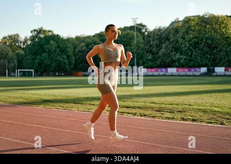Sportliche junge Frau in Sportbekleidung, die bei Sonnenuntergang auf der Stadionbahn läuft. Konzept von Fitness, Entschlossenheit und aktivem Lebensstil. Stockfoto
